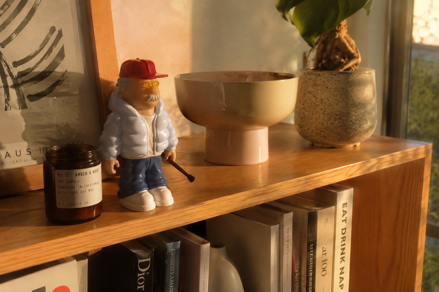 GRMP en una estantería de madera con luz cálida de tarde, junto a una vela y libros de diseño